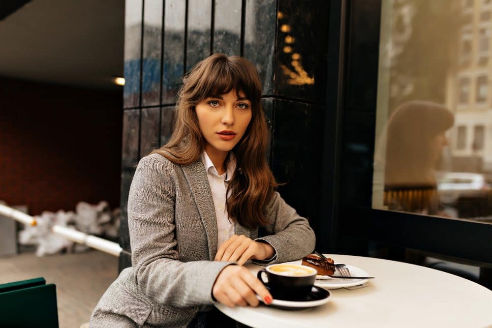 gri paltolu, kahküllü göz alıcı bir kadın, cafe'de oturuyor ve kahve molası veriyor=